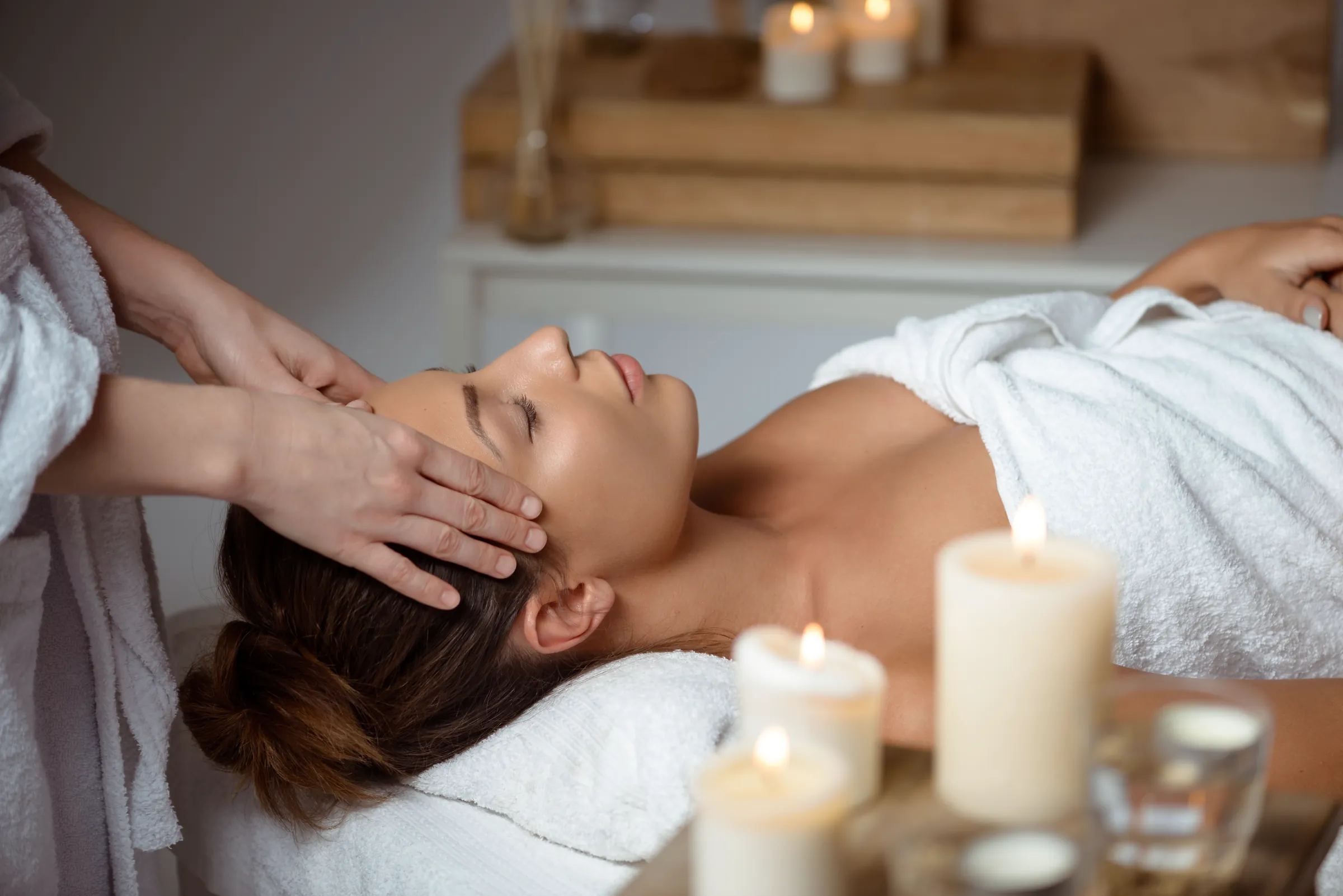 A practitioner’s hands gently rest on a relaxed client’s forehead during a facial treatment