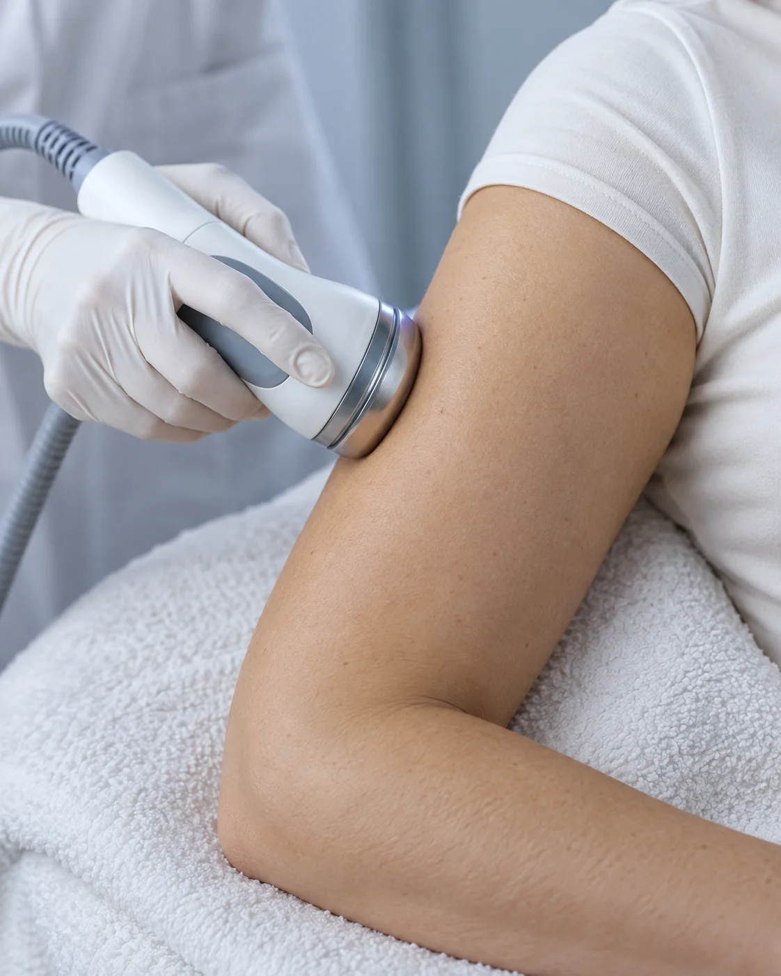 A gloved hand holding a round treatment handpiece against a client’s upper arm