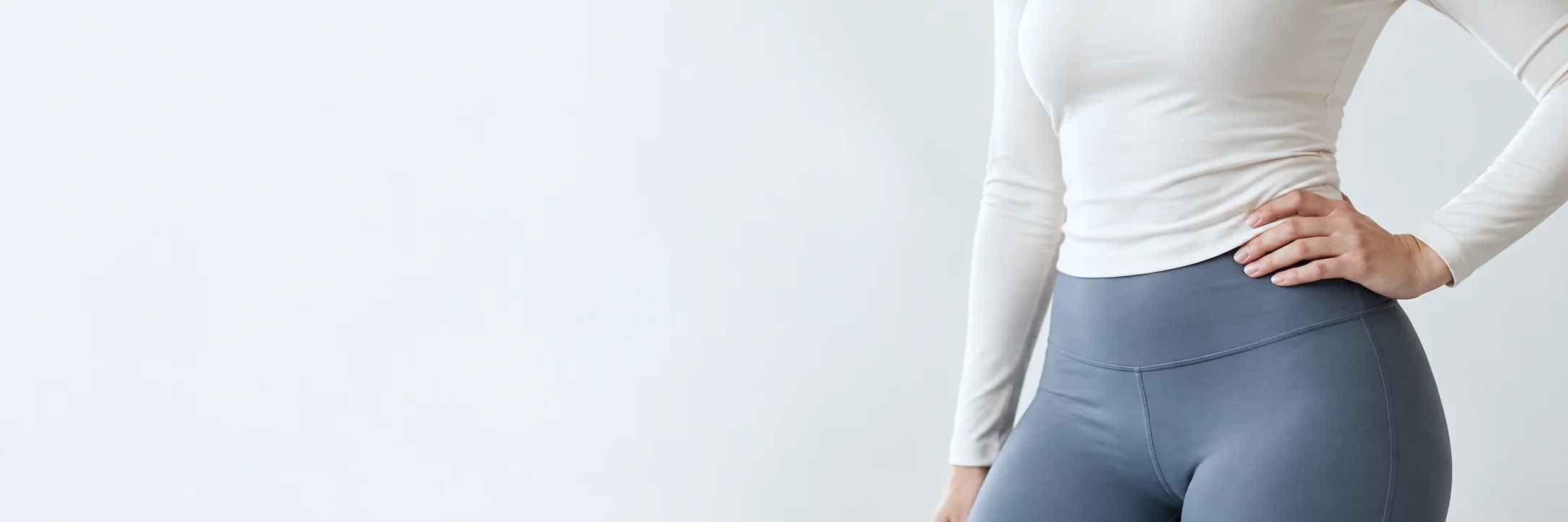 A woman’s waist in an ivory fitted top and slate-blue leggings, one hand resting on her hip