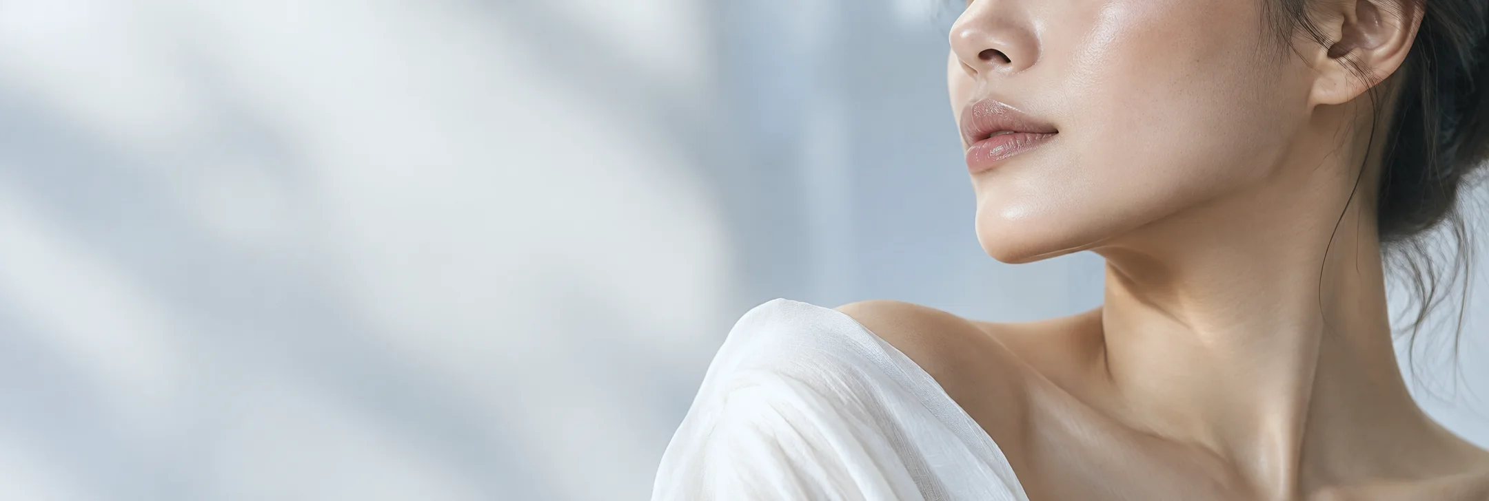 Soft-light profile of a woman’s lower face, neck and shoulder against a pale ivory background