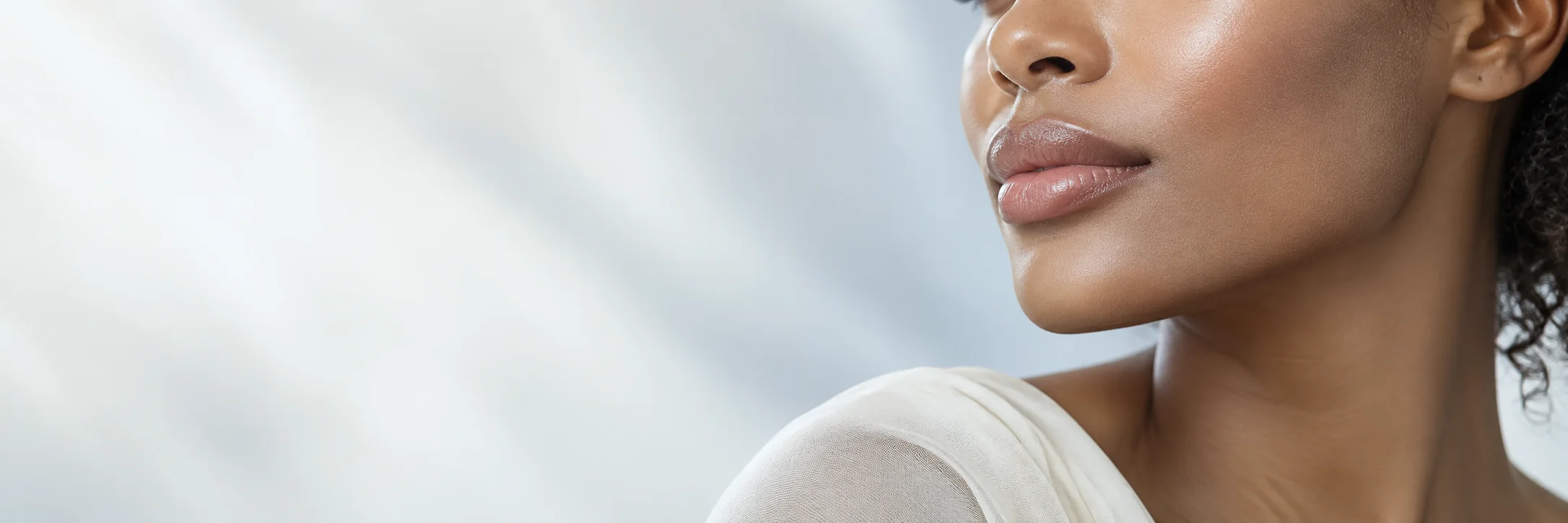 Soft-light profile of a woman’s lower face and jaw against a pale ivory background