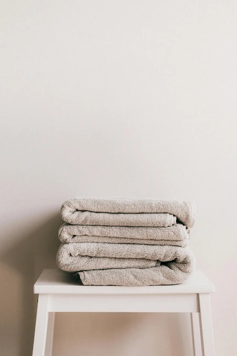 Neatly folded towels on a white stool against a warm neutral wall