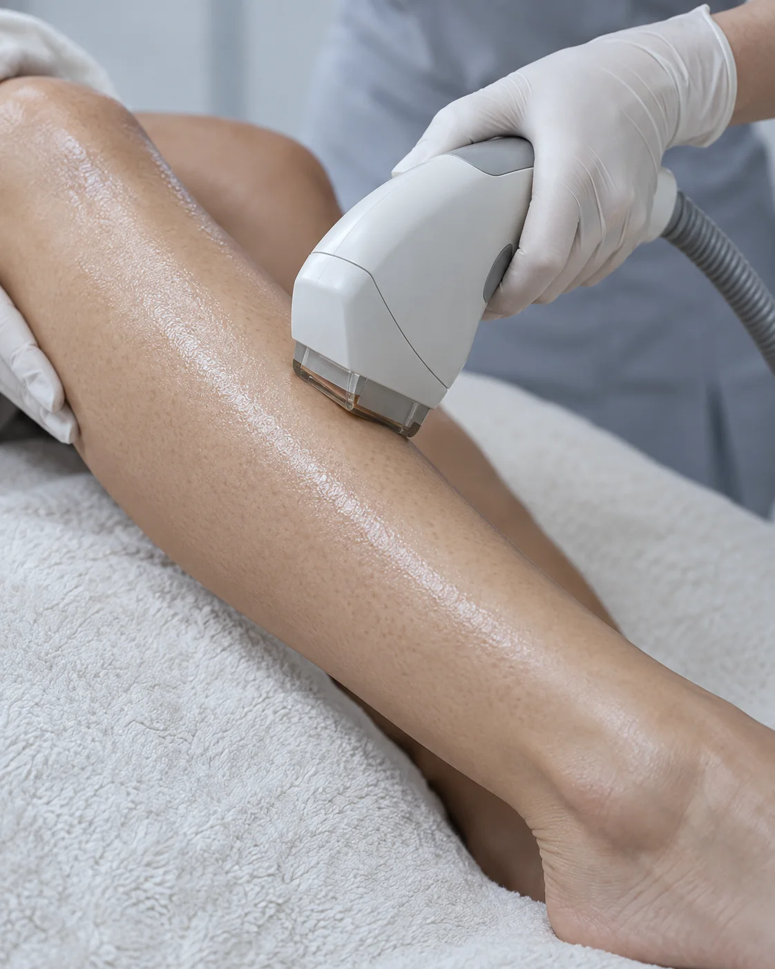 A gloved hand holding a rectangular treatment handpiece against a client’s lower leg