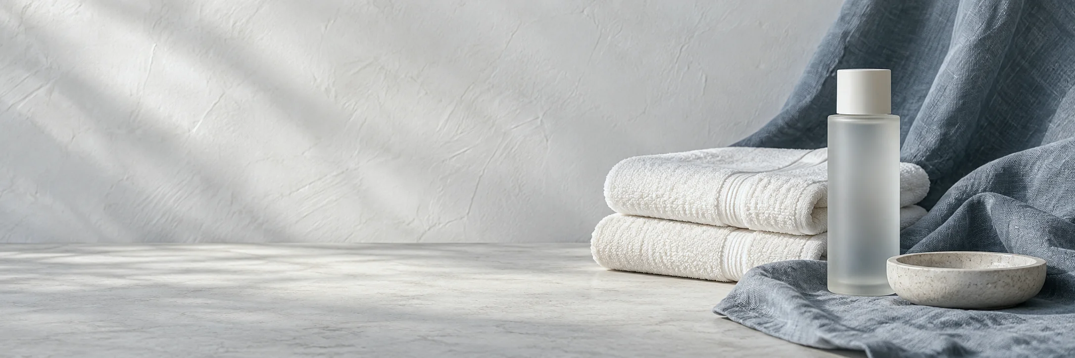Folded white towels, a frosted bottle and a stone dish on slate-blue linen