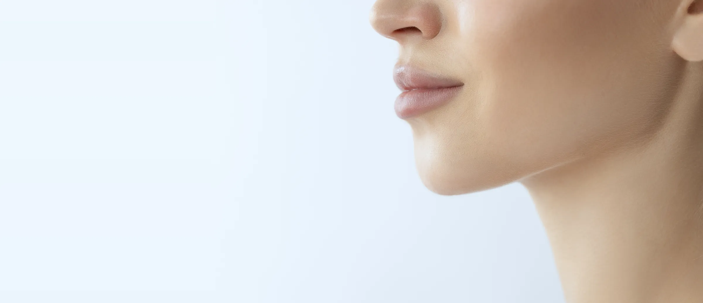 Close profile of a woman’s lips, jaw and neck against a pale background