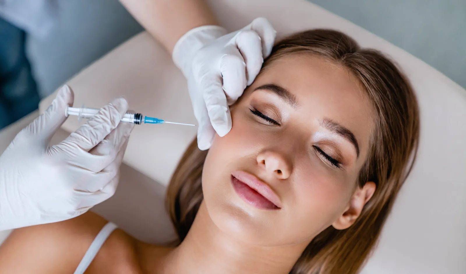 Gloved hands holding a syringe near a relaxed client’s temple