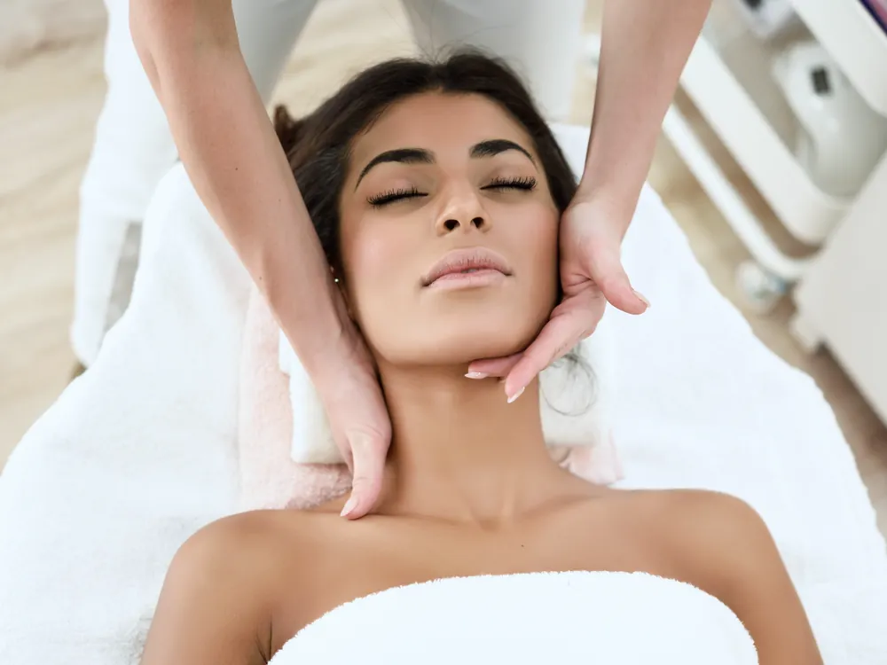A relaxed client with eyes closed as a practitioner’s hands frame her face