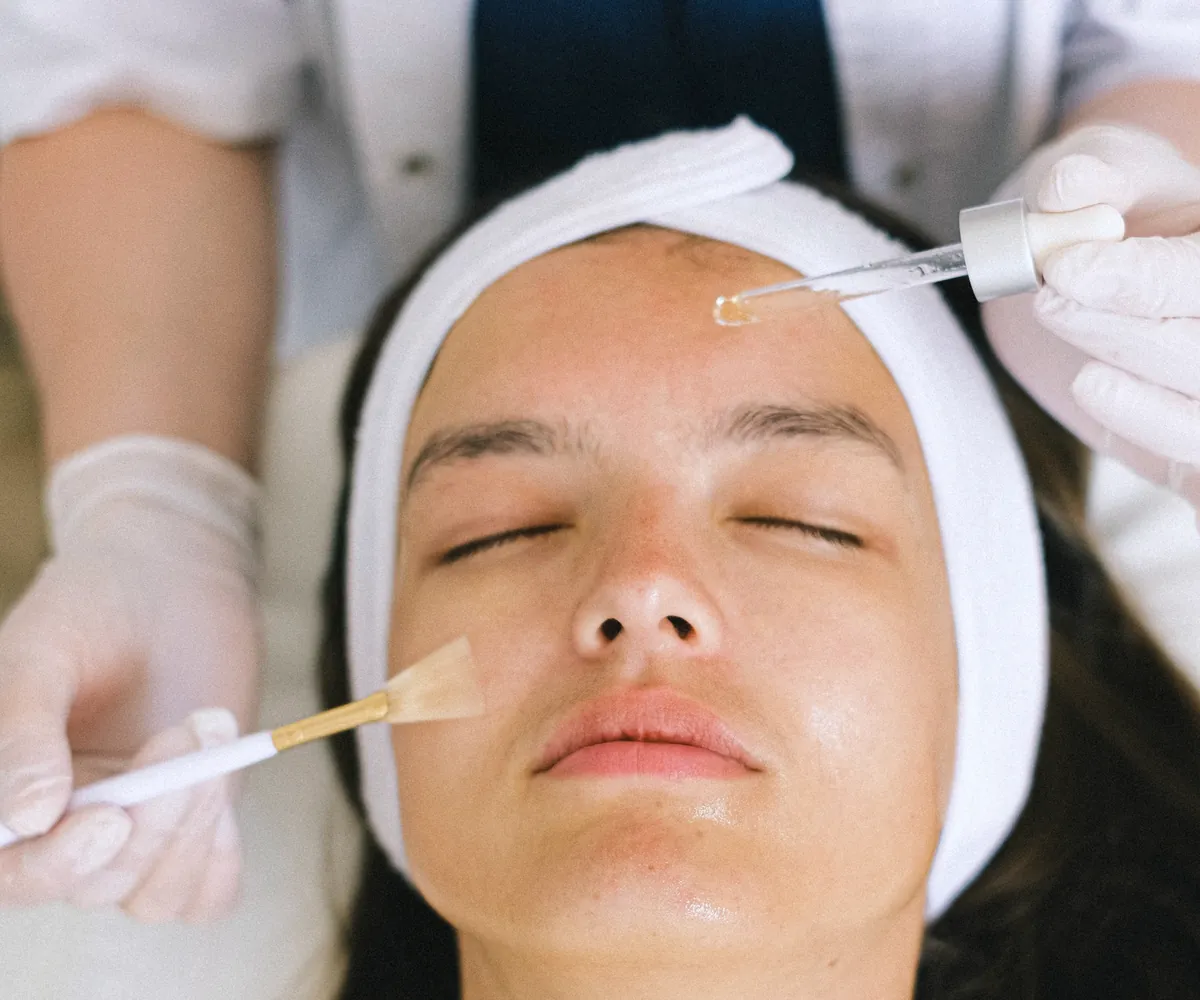 A gloved hand brushing a treatment solution onto a client’s cheek