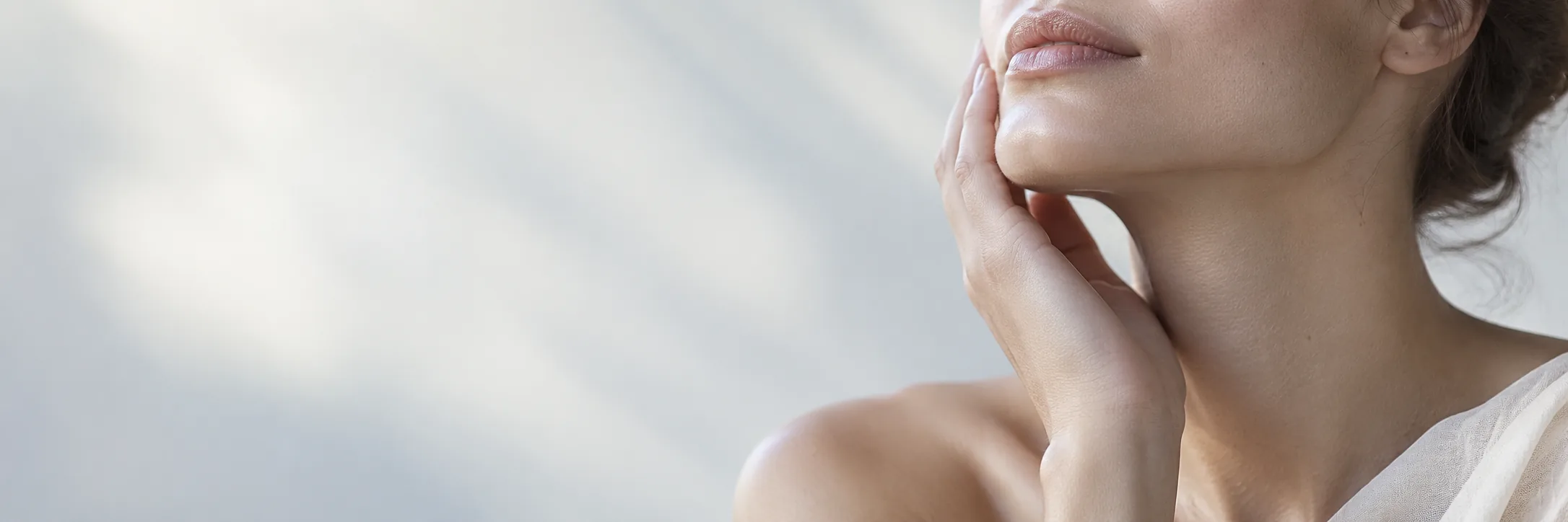 Close-up of a hand resting softly against the jaw and neck in diffused light