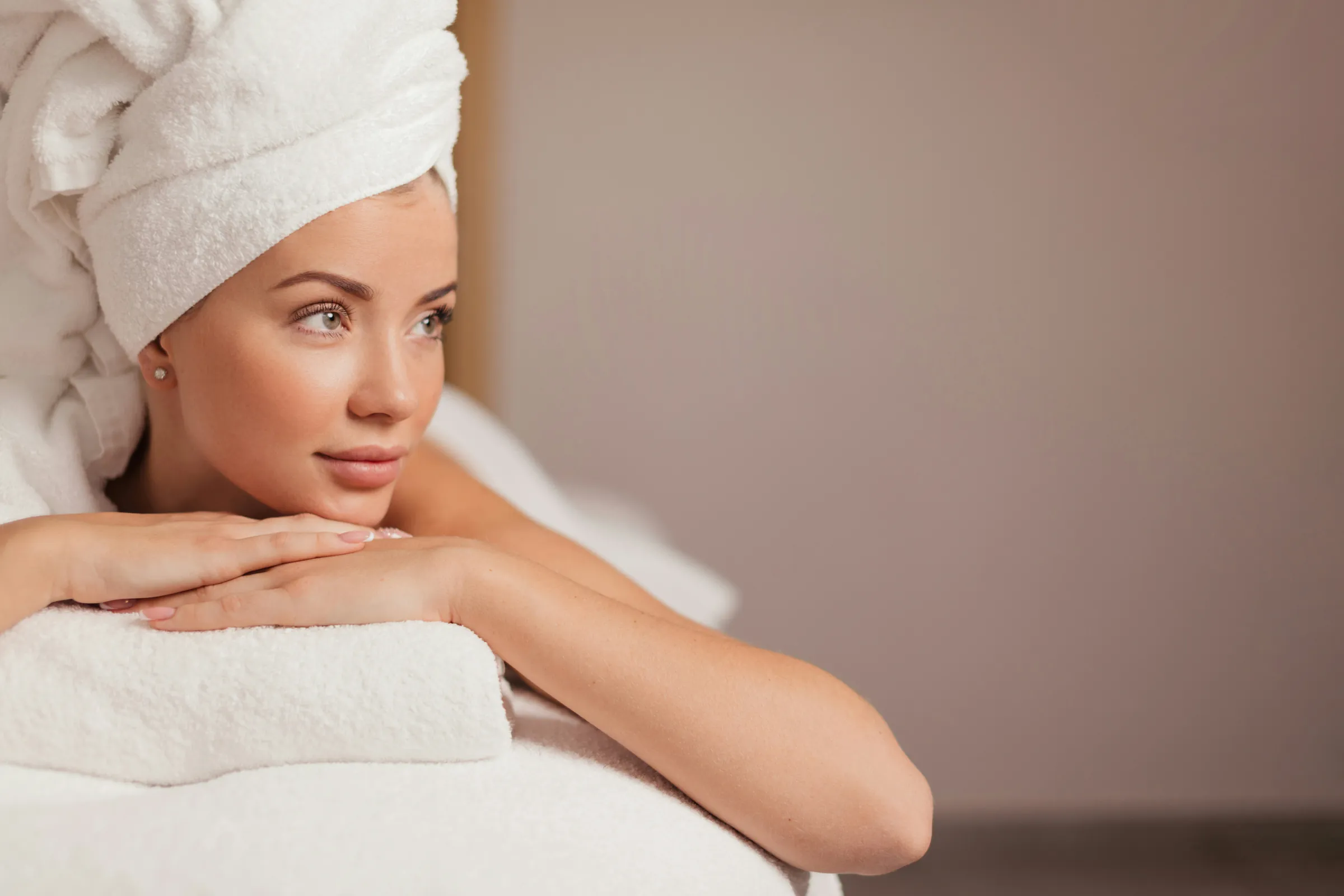 A woman in a white towel wrap rests her chin on her hands, her skin fresh and glowing